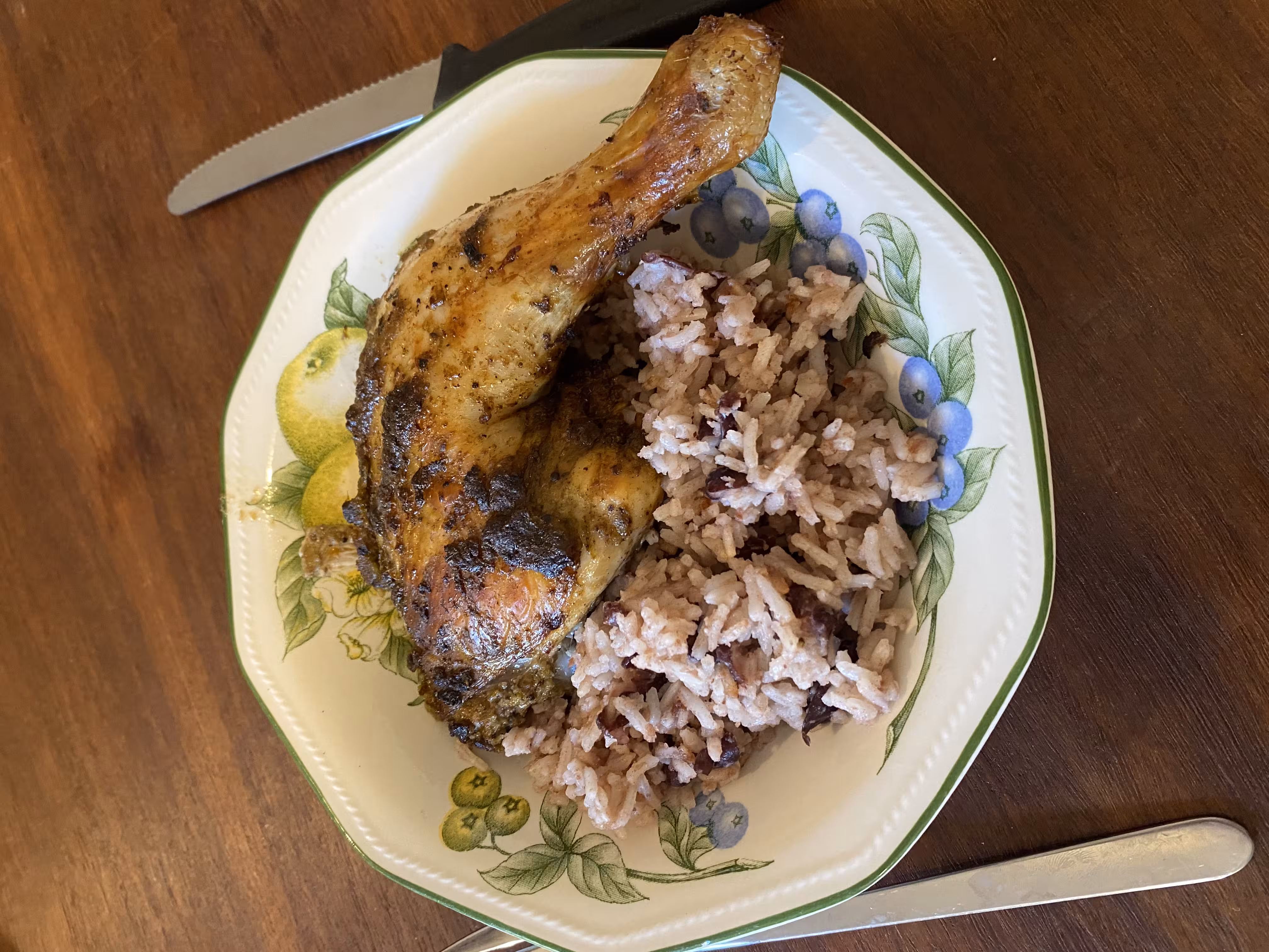 Bowl of jerk chicken with side of rice and peas